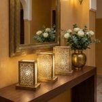 Three brass lantern table lamps in graduated sizes on console table with white roses in luxury hotel lobby