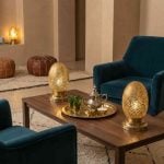 Brass oval table lamps on coffee table in elegant living room with leather poufs and tea service