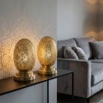 Two brass oval table lamps on modern console table casting decorative shadows in contemporary living space