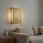 Brass mandala wall light with glowing side panel casting sunburst shadow pattern on living room wall above sofa