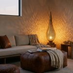 Hand-pierced brass floor lamp casting warm geometric shadows in a modern living room with a rich brown leather ottoman.