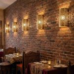 Row of Moroccan brass filigree wall sconces illuminating exposed brick wall in restaurant
