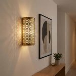 Moroccan brass filigree wall light casting intricate lace shadow patterns in modern hallway