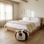 Natural cowhide round ottoman at foot of oak bed in minimalist bedroom with chunky knit blanket