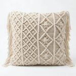 Cream macrame cushion cover featuring intricate diamond and leaf knotwork patterns with decorative side fringe tassels