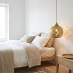 Brass fish scale pendant lamp hanging beside a linen bed in a bright minimalist bedroom