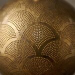Close-up of hand-pierced dots and engraved fan outlines on a raw brass pendant shade