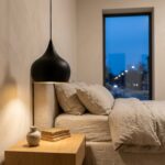 Black teardrop pendant light used as a bedside lamp beside a linen bed