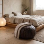 Brown leather pouf with a knit throw at the foot of a low oak bed