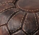 Close-up of hand-dyed goatskin panels with cream hand stitching on a brown pouf