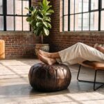 Brown leather pouf used as a footrest in a brick-walled loft