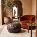 Brown leather pouf on a cream wool rug beside a rust velvet armchair in a riad