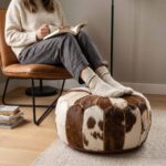 Brown and white cowhide pouf used as a footrest in front of a cognac leather chair