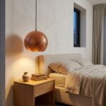 Hammered copper pendant light used as a bedside lamp beside a linen bed