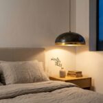 Hammered copper pendant light with gold leaf band hanging beside a bed