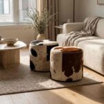 Two round cowhide ottomans, black & white and brown & white, on a wool rug beside a boucle sofa and travertine coffee table