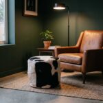 Black and white cowhide ottoman in front of a tan leather armchair in a green reading room