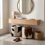 Black & white and brown & white cowhide ottomans under a floating oak console in an entryway