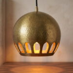 Close-up of hand-hammered brass globe pendant with arched cutouts glowing warm gold