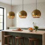 Three hammered brass globe pendant lights over a travertine kitchen island