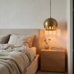 Brass globe pendant light hanging beside a linen bed over an oak nightstand