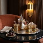 Hand-painted glass tea set served on engraved tray on a black marble table beside dates