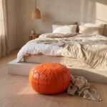 Orange leather pouf at the foot of a platform bed with linen bedding