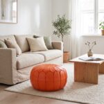 Orange leather pouf on a wool rug beside a linen sofa and oak coffee table