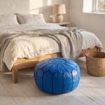 Royal blue leather pouf at the foot of an oak bed next to a woven straw basket
