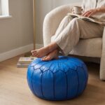 Royal blue leather pouf used as a footrest in a reading corner with a boucle armchair