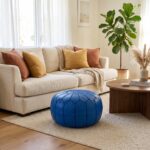 Royal blue leather pouf on a cream rug in front of a sofa with mustard and rust cushions