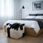 Black and white square cowhide ottoman at the foot of a bed
