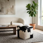 Black and white cowhide pouf beside a walnut coffee table and cream sofa