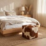 Brown and white cowhide ottoman at the foot of a linen-dressed bed