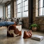 Brown and white cowhide pouf used as a footrest in an industrial loft
