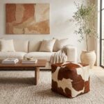 Brown and white square cowhide pouf beside a sofa and walnut coffee table
