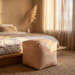 Undyed square leather pouf at the foot of a linen-dressed bed in warm evening light